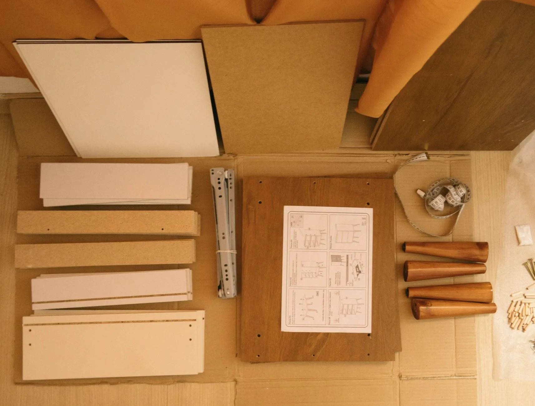 Flat-pack furniture panels, rails, legs and the instruction sheet laid out on a cardboard sheet