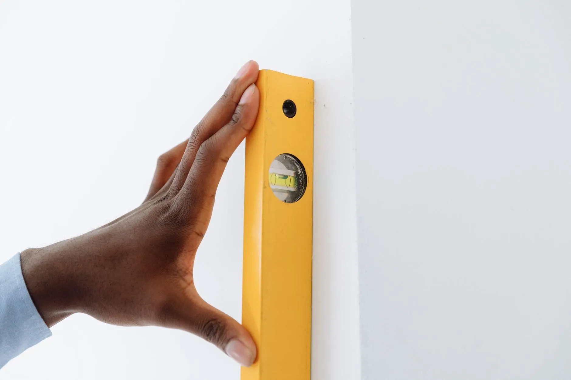 A hand holding a yellow spirit level flat against a white wall