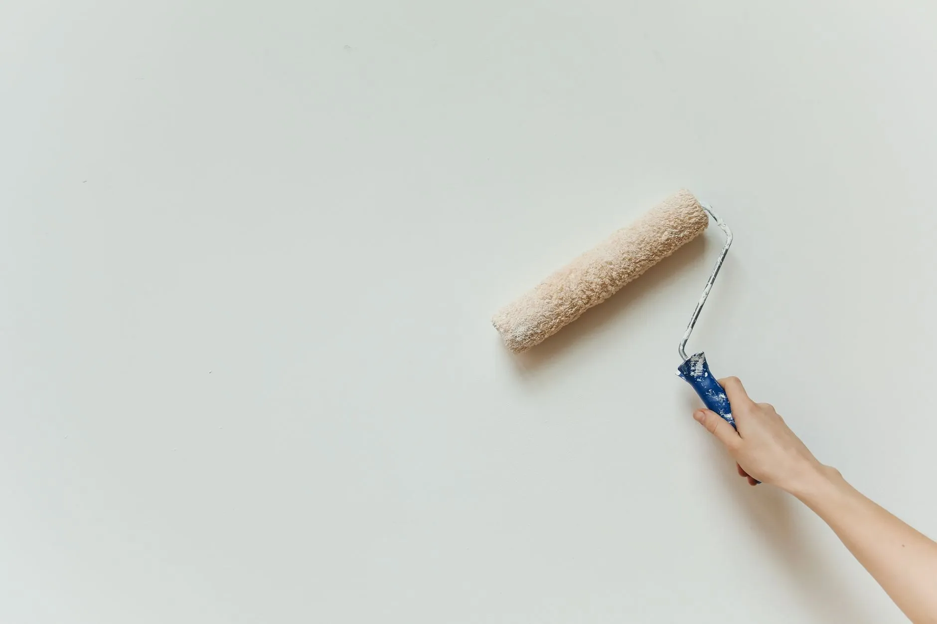 A hand rolling paint onto a smooth off-white wall