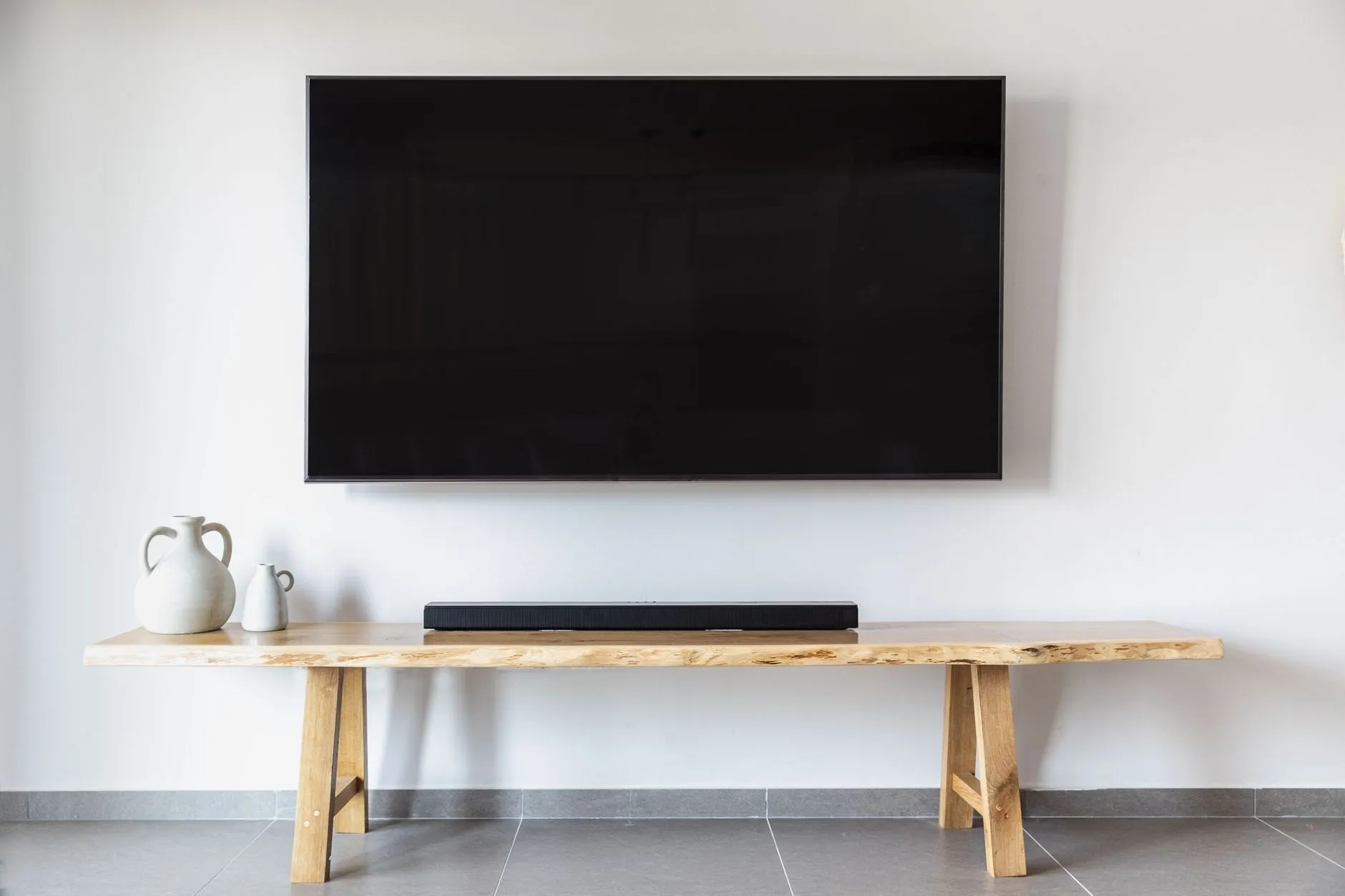 A large flat-screen TV mounted on a white wall above a live-edge timber bench