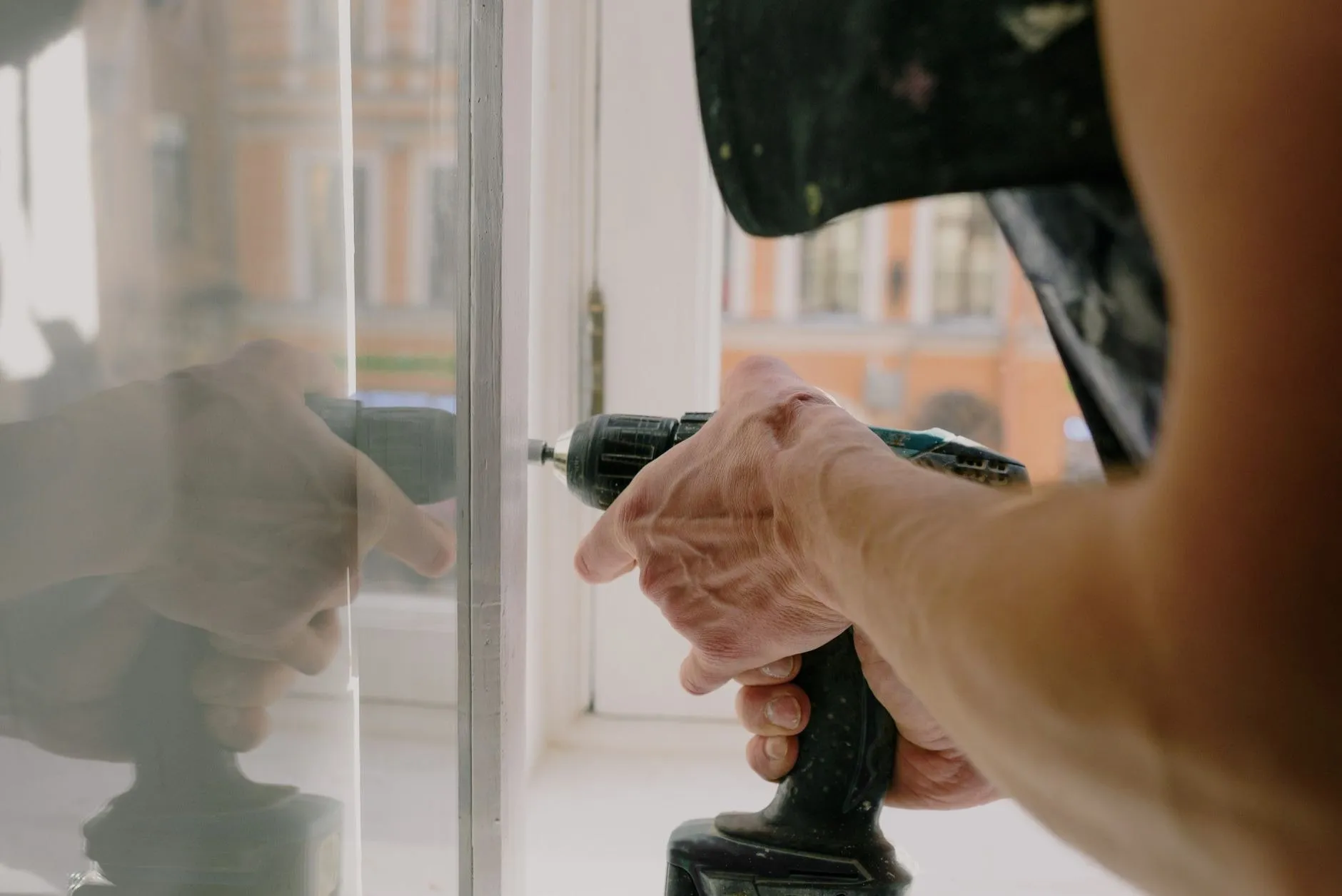 Close-up of hands driving a screw into a window frame hinge